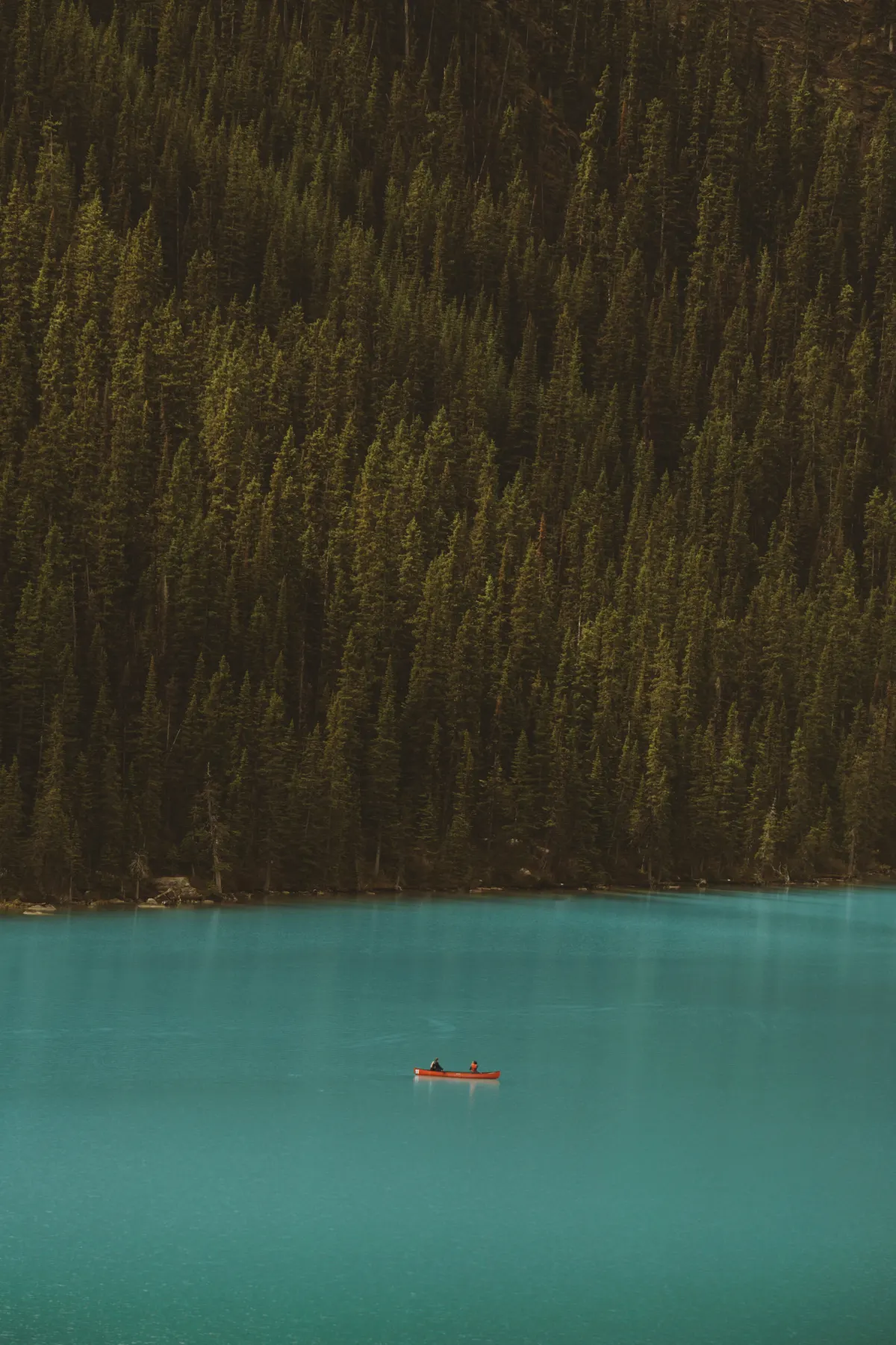 Two people canoeing on an emerald lake beneath a forested hillside.