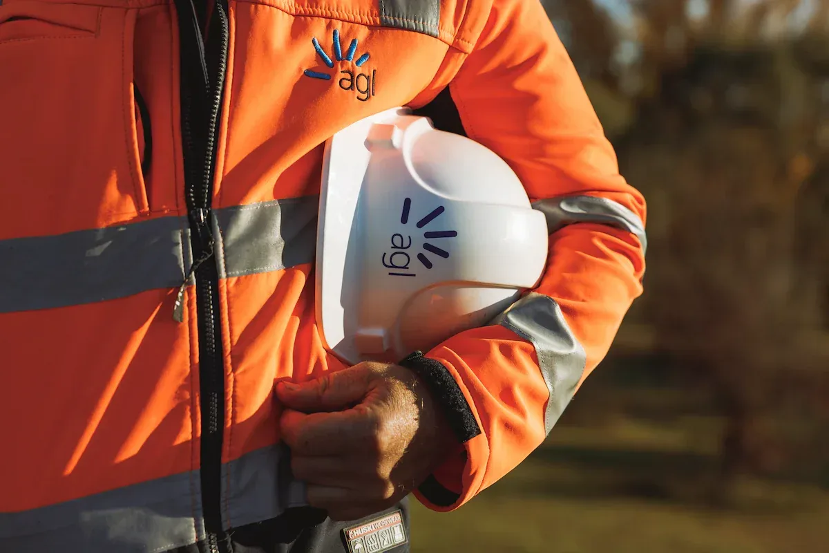 AGL field worker in hi-vis carrying a branded hard hat under one arm.