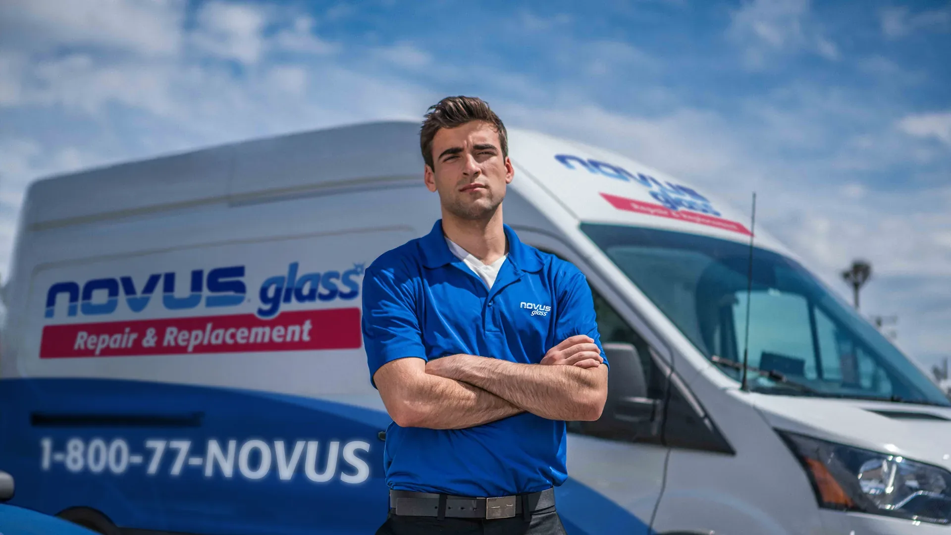 Novus Glass technician standing with arms crossed in front of a branded repair van